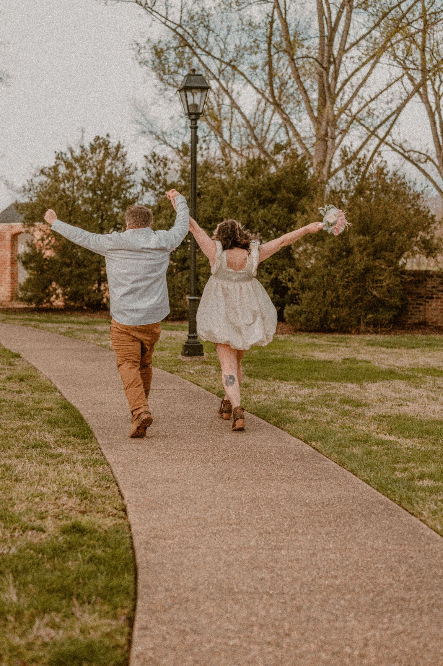 A joyful eloping couple runs down a pathway with arms outstretched in celebration. photo by Samantha Campbell imagery