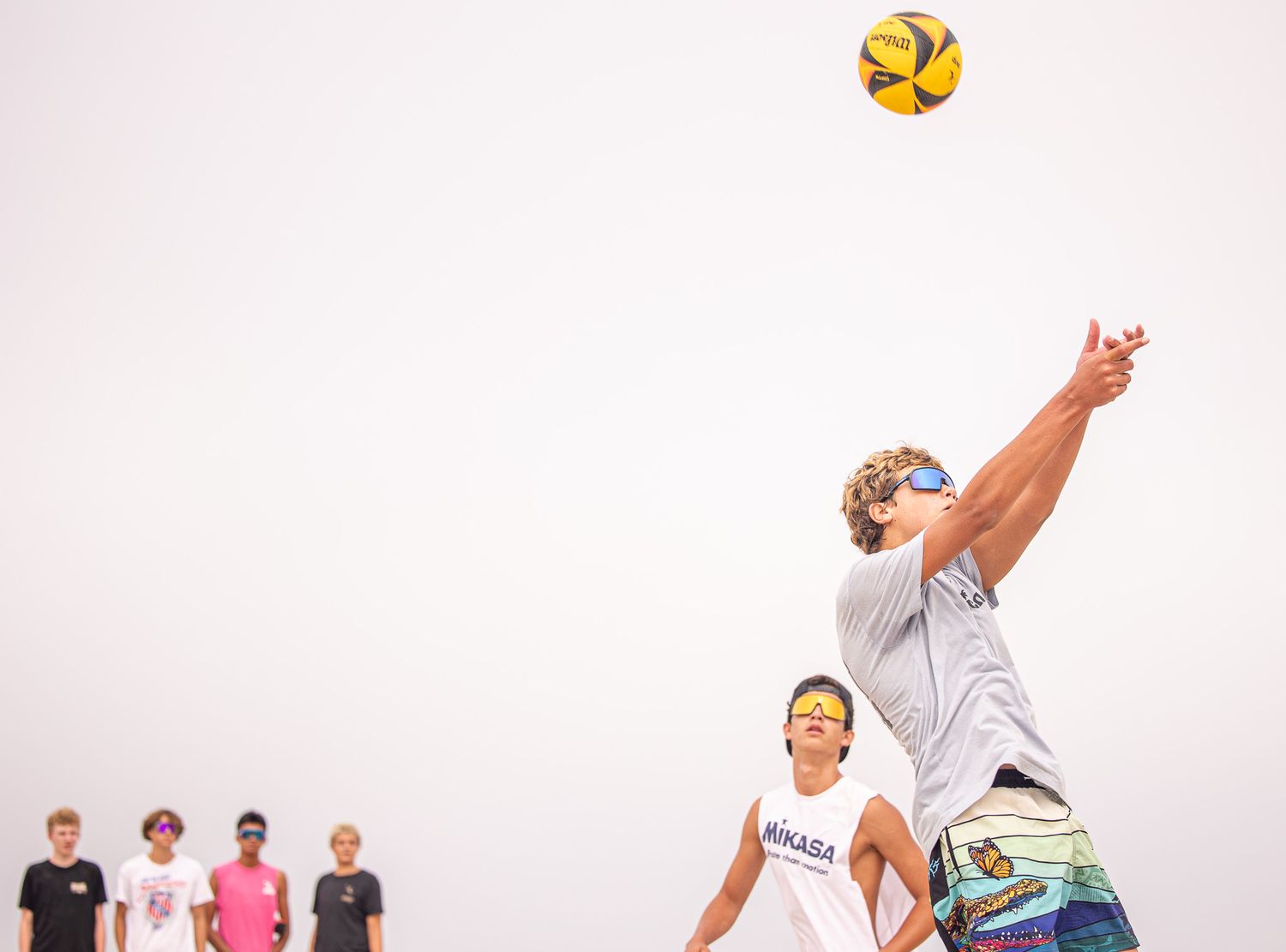 Beach volleyball players leaping to hit yellow ball during competitive match.
