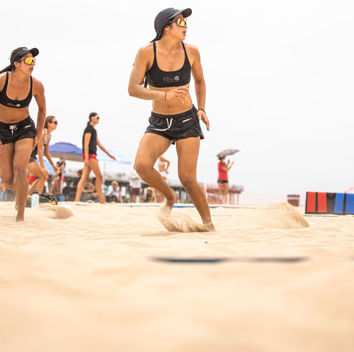 Athletes running on sandy beach volleyball court during competition.