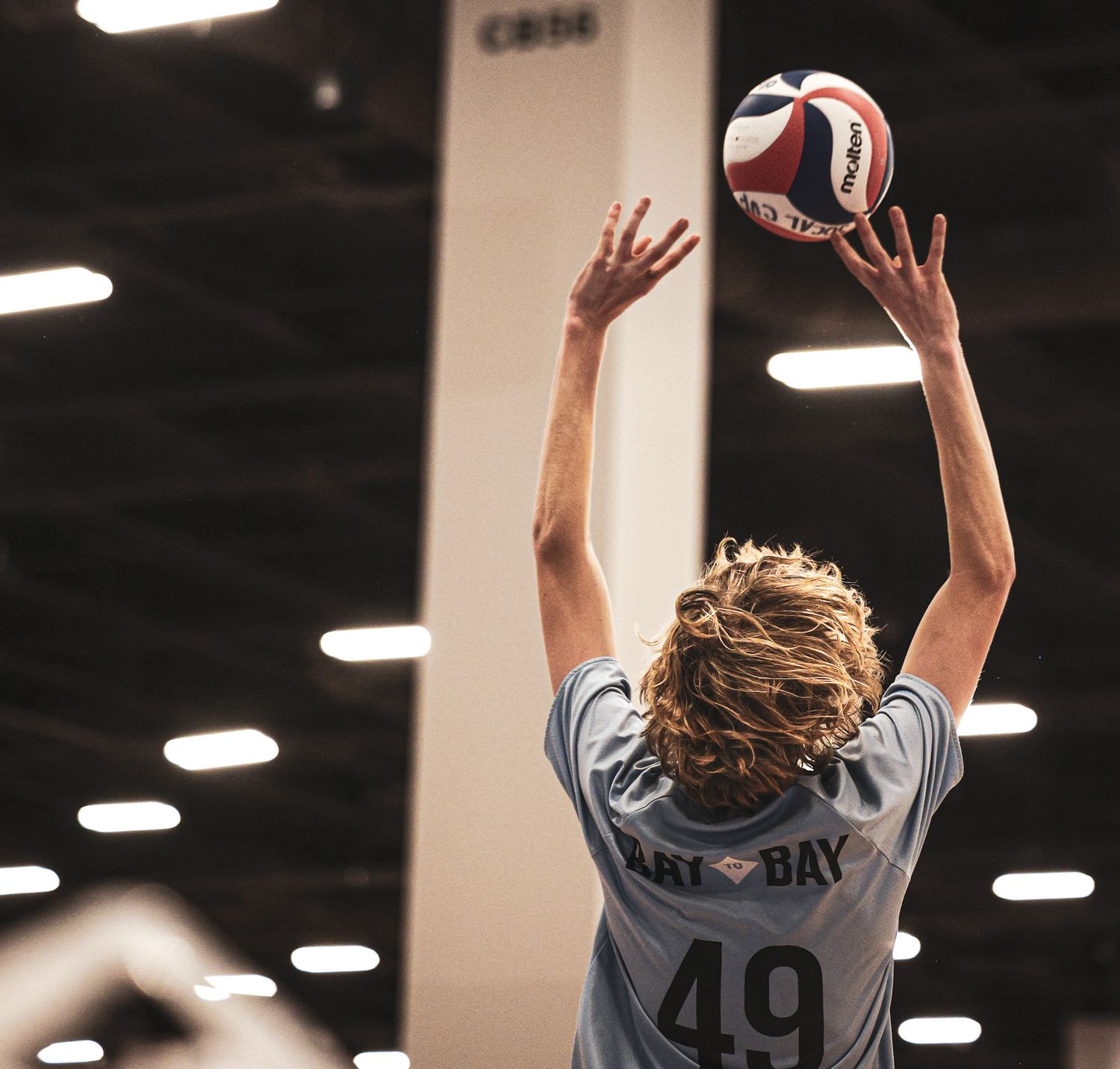 Volleyball player in a grey jersey numbered 49 reaches up to set the ball during an indoor match.