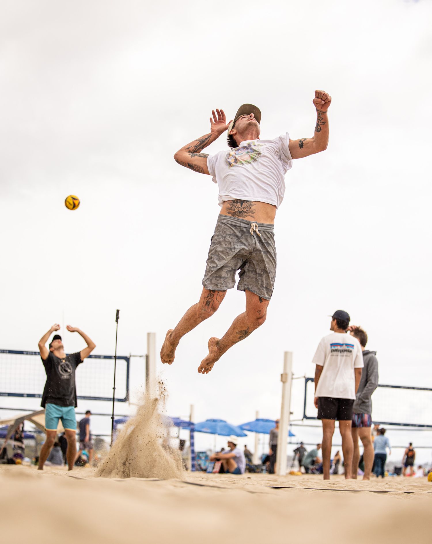 Beach volleyball player jumping high to spike the ball during an outdoor game on a sandy court.