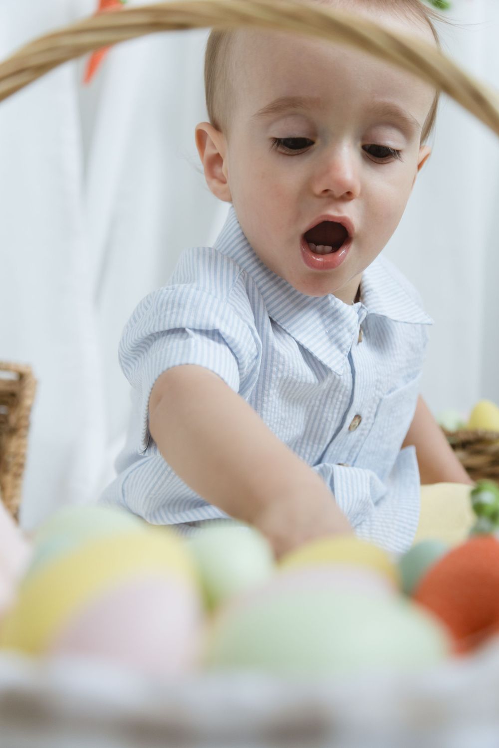 Small child in striped shirt reaching for colorful Easter eggs in a festive spring setting.