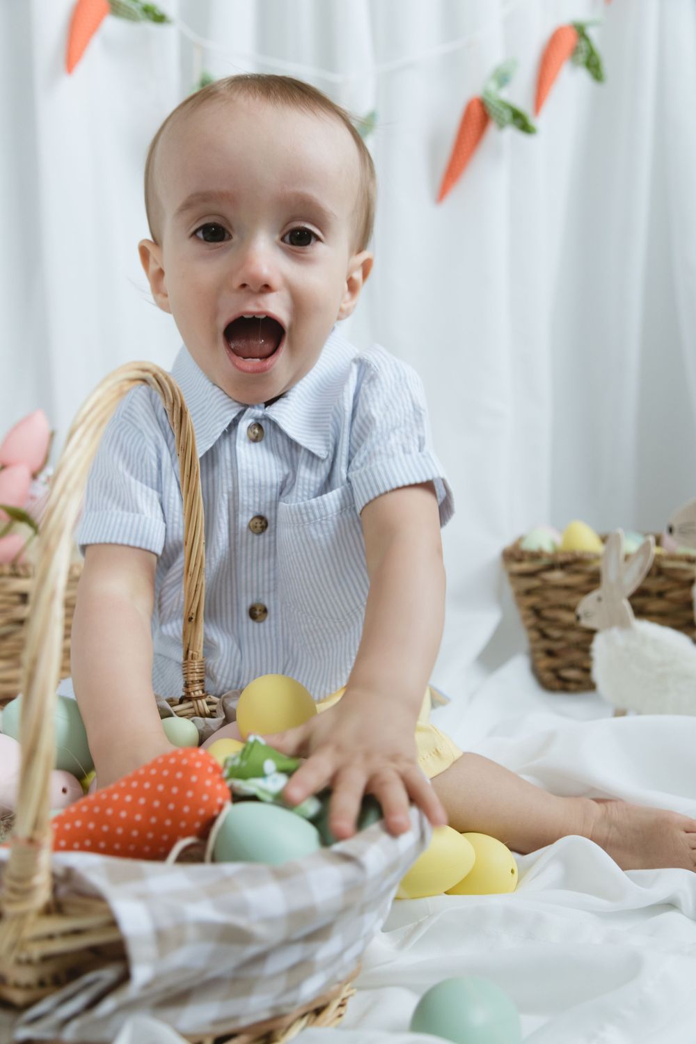 Easter themed photo setup with carrot banner, colorful eggs and wicker baskets against white background.