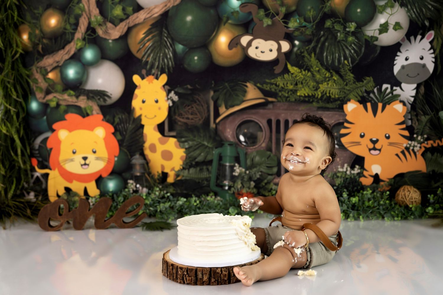 Safari-themed first birthday setup with colorful jungle animal decorations and a simple white cake on wooden slice.