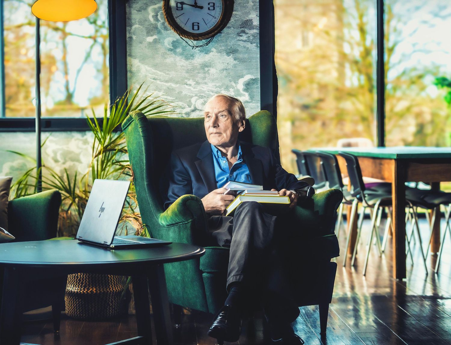 Senior man in blue blazer sits thoughtfully in sunny restaurant interior.