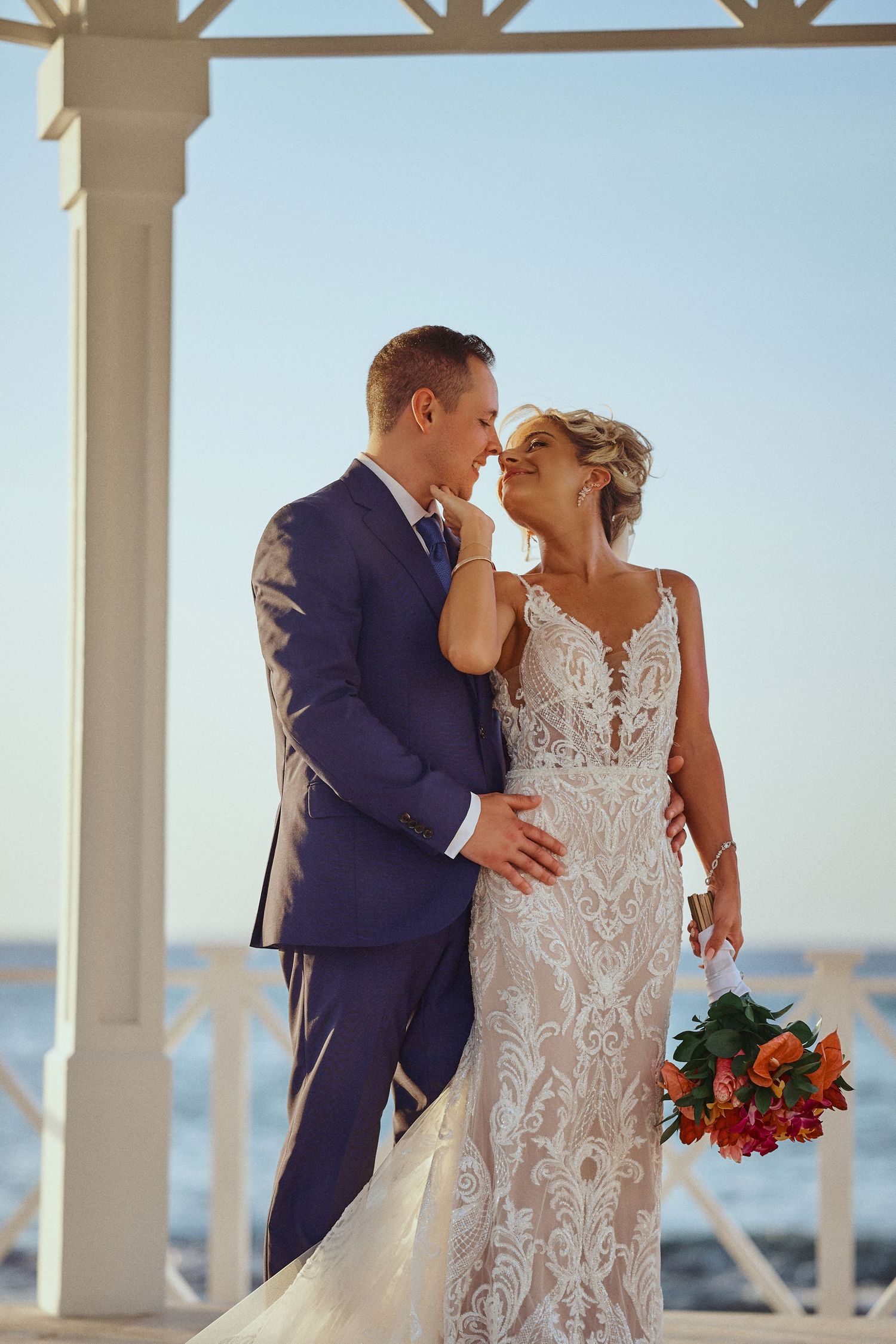 A romantic couple embraces while standing in ocean water at sunset with a boat silhouette. Jamaica Wedding Photographer