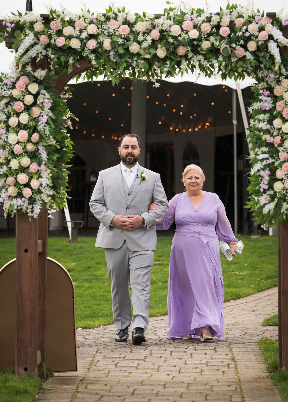 A beautifully decorated floral arch with pink and white roses frames the entrance to a wedding venue.