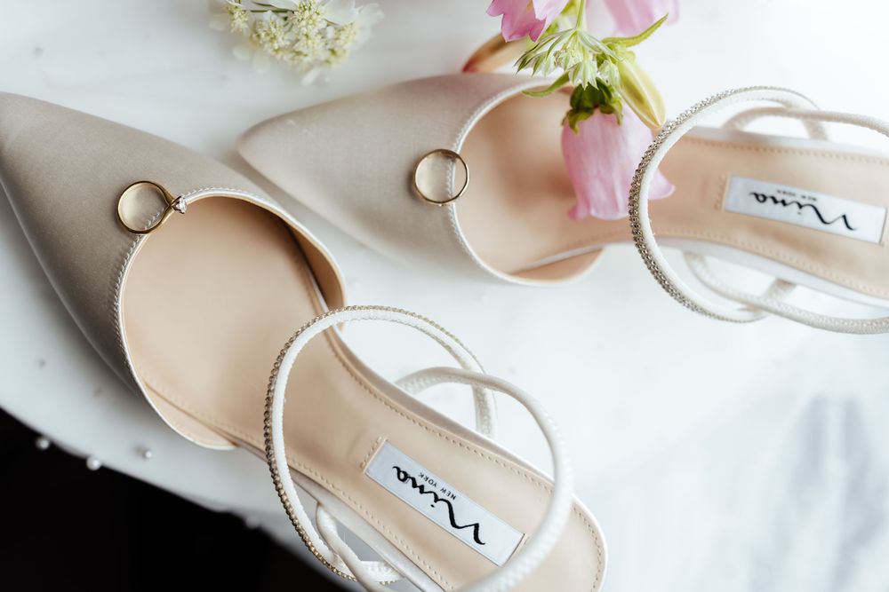 Elegant nude pointed bridal shoes with wedding rings and delicate pink flowers.
