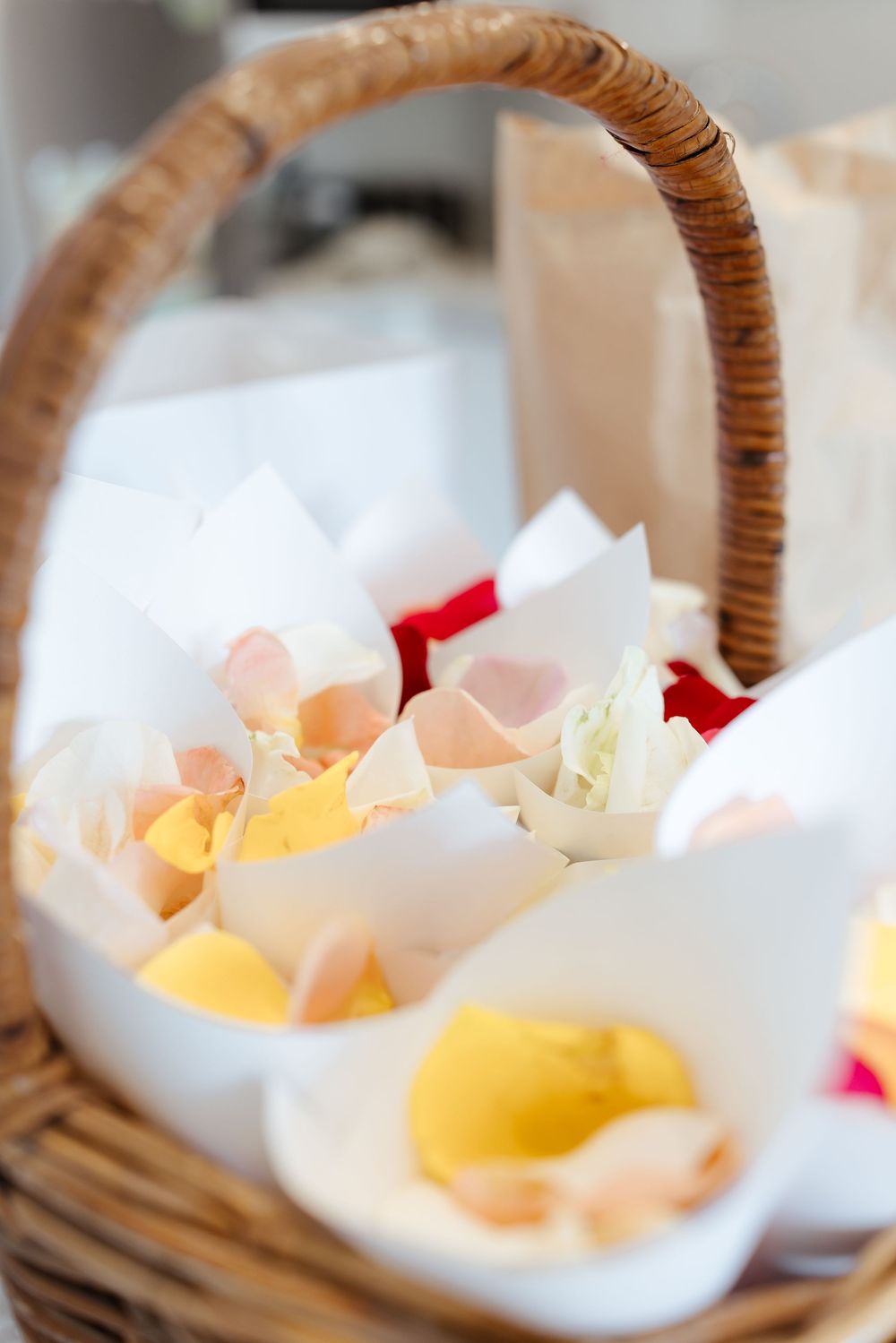 Wicker basket filled with delicate flower petals in white, yellow and pink tones.