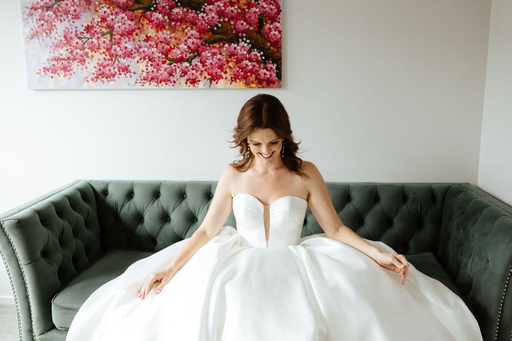Bride posing on teal velvet couch with pink floral artwork in background.