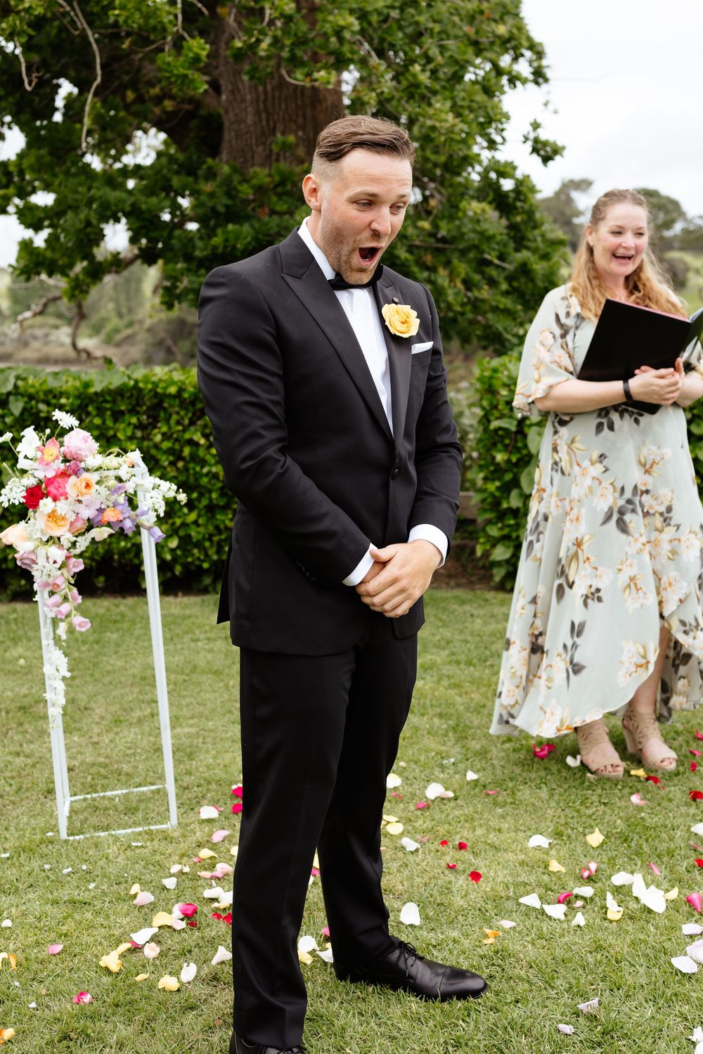 Wedding ceremony setup on grass lawn with scattered rose petals and white chairs.