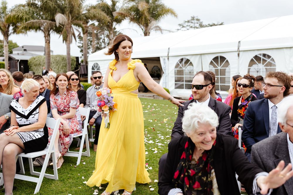 Wedding guests celebrate outdoors with yellow and floral dresses under a white tent.