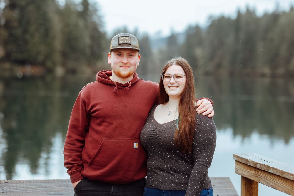 Couple in casual attire pose together on wooden dock by serene lake.