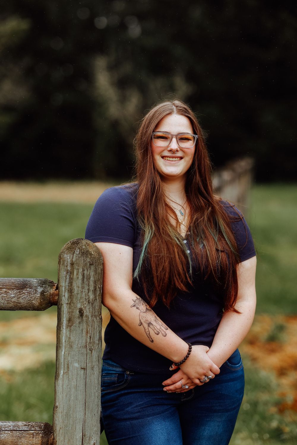 Person in navy shirt poses casually against wooden fence in natural outdoor setting.