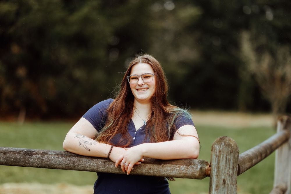 Person smiling while leaning on rustic wooden fence rail outdoors.