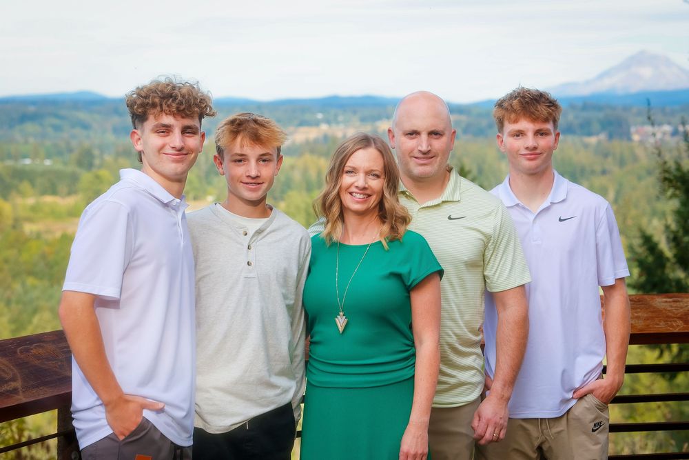 Family poses together outdoors with mountains and green landscape in the background on a sunny day.