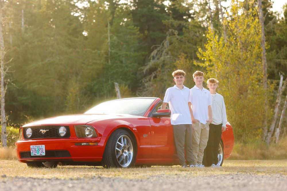 A red Ford Mustang GT parked near a forest with autumn foliage in golden sunlight.
