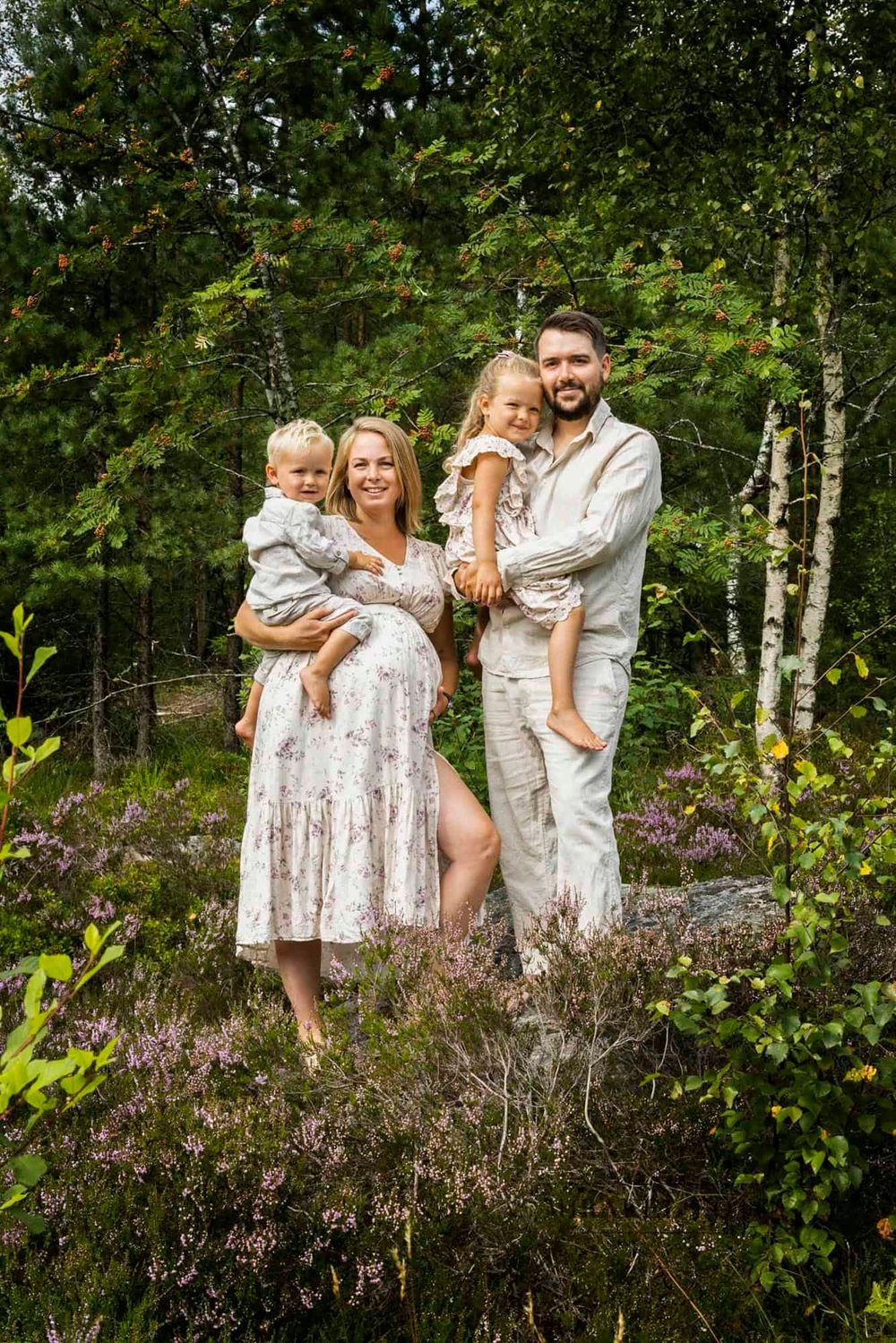 Familie på 4 med gravid mamma som står på en høyde i Lyngdal i sommerklær og smiler ned mot fotografen