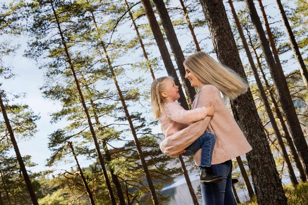 Mamma som holder 4 år gammel jente og har det gøy mens de snurrer rundt i skogen på familifotografering i Farsund