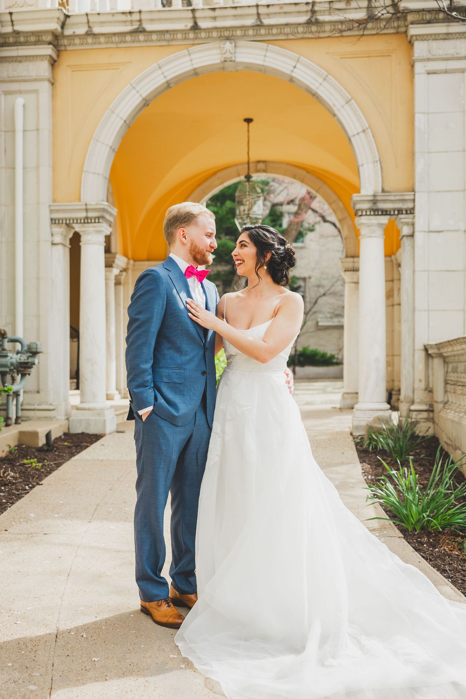 Elegant wedding couple poses beneath yellow arched colonnade with classical architecture at Josephine Butler Parks Center