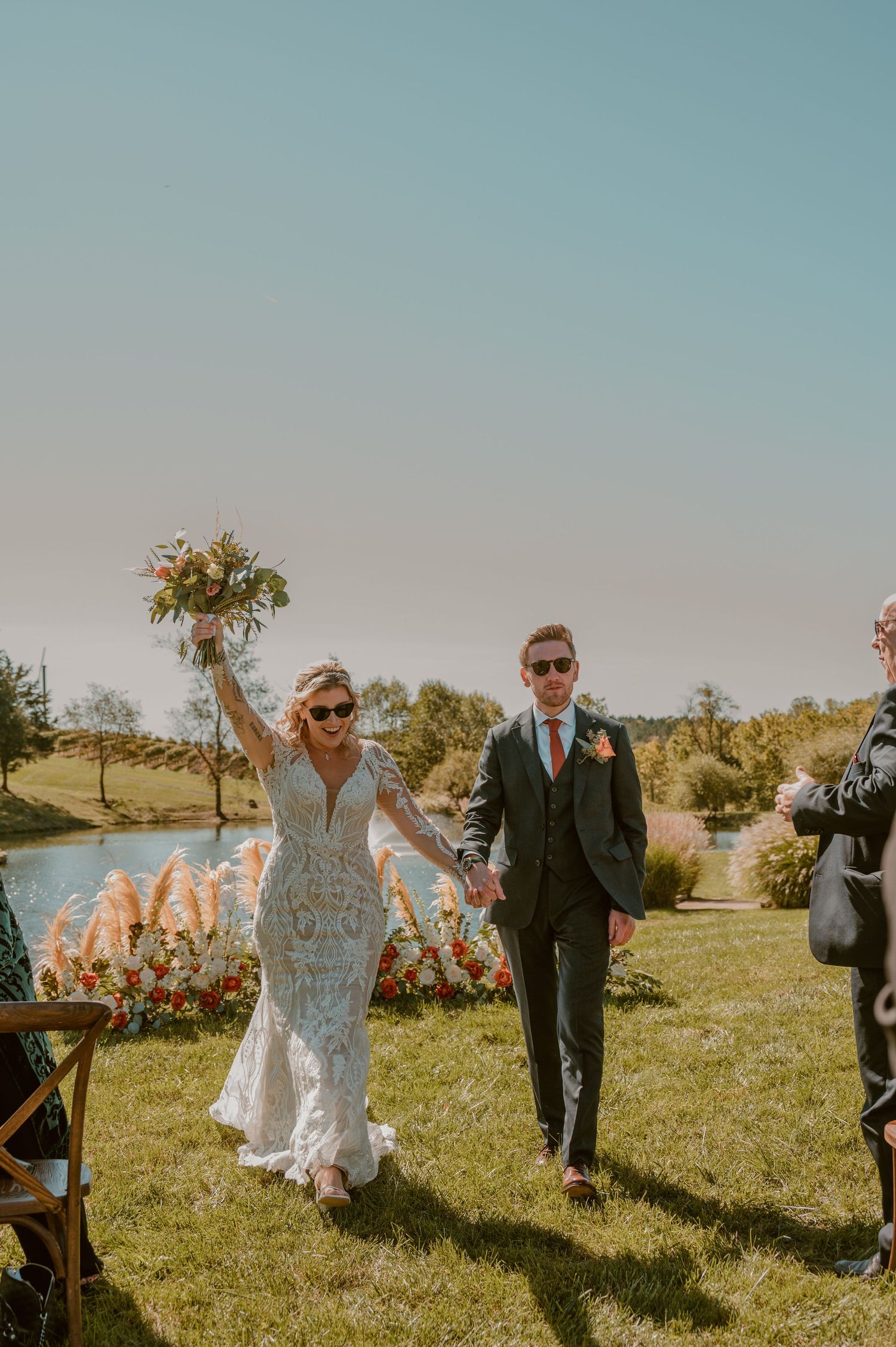 A happy couple celebrates their outdoor wedding ceremony on a scenic hillside with pampas grass decor and golden sunlight. Samantha Campbell
