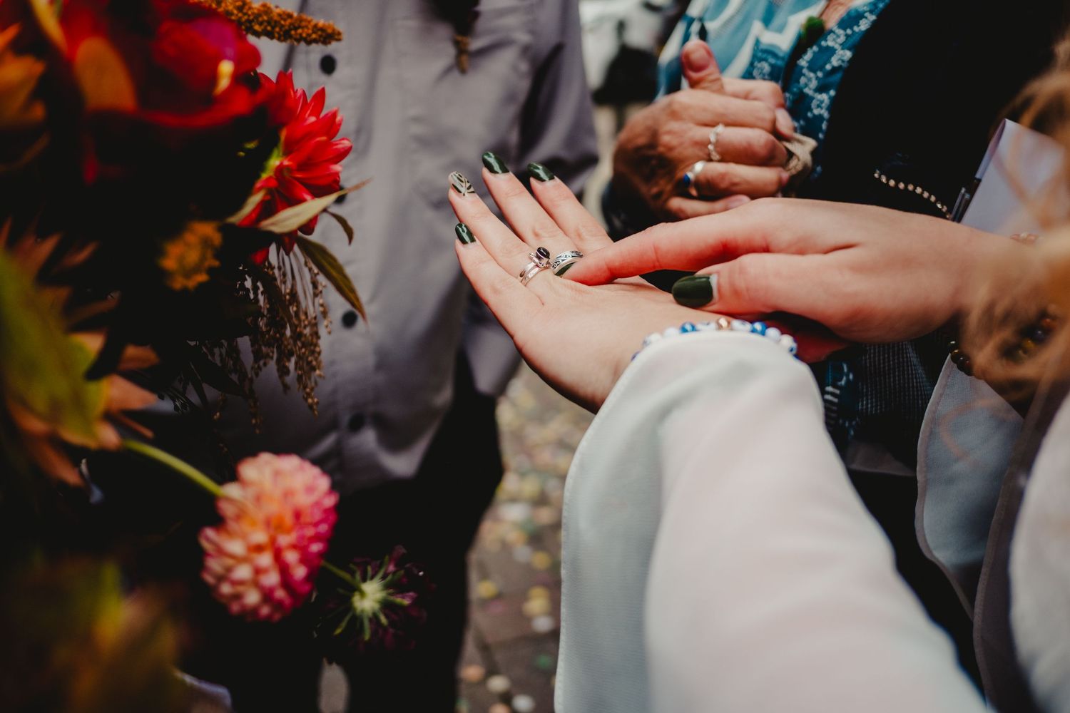 Hands engaging in a wedding or commitment ceremony with colorful autumn flowers in the background.