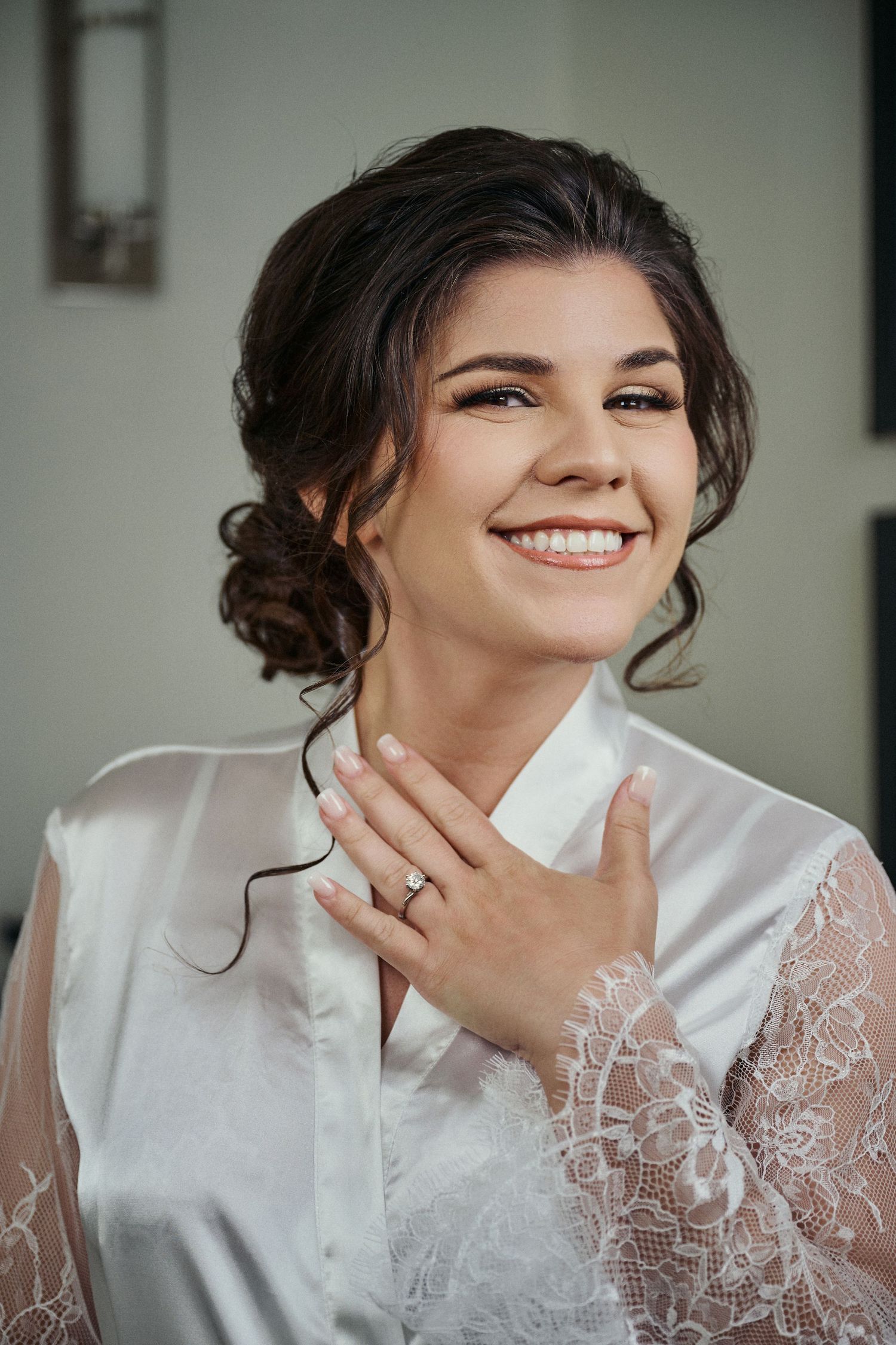Portrait of a bride getting ready in silk robe with lace sleeves, smiling with an updo hairstyle and engagement ring. Jamaican Photographer