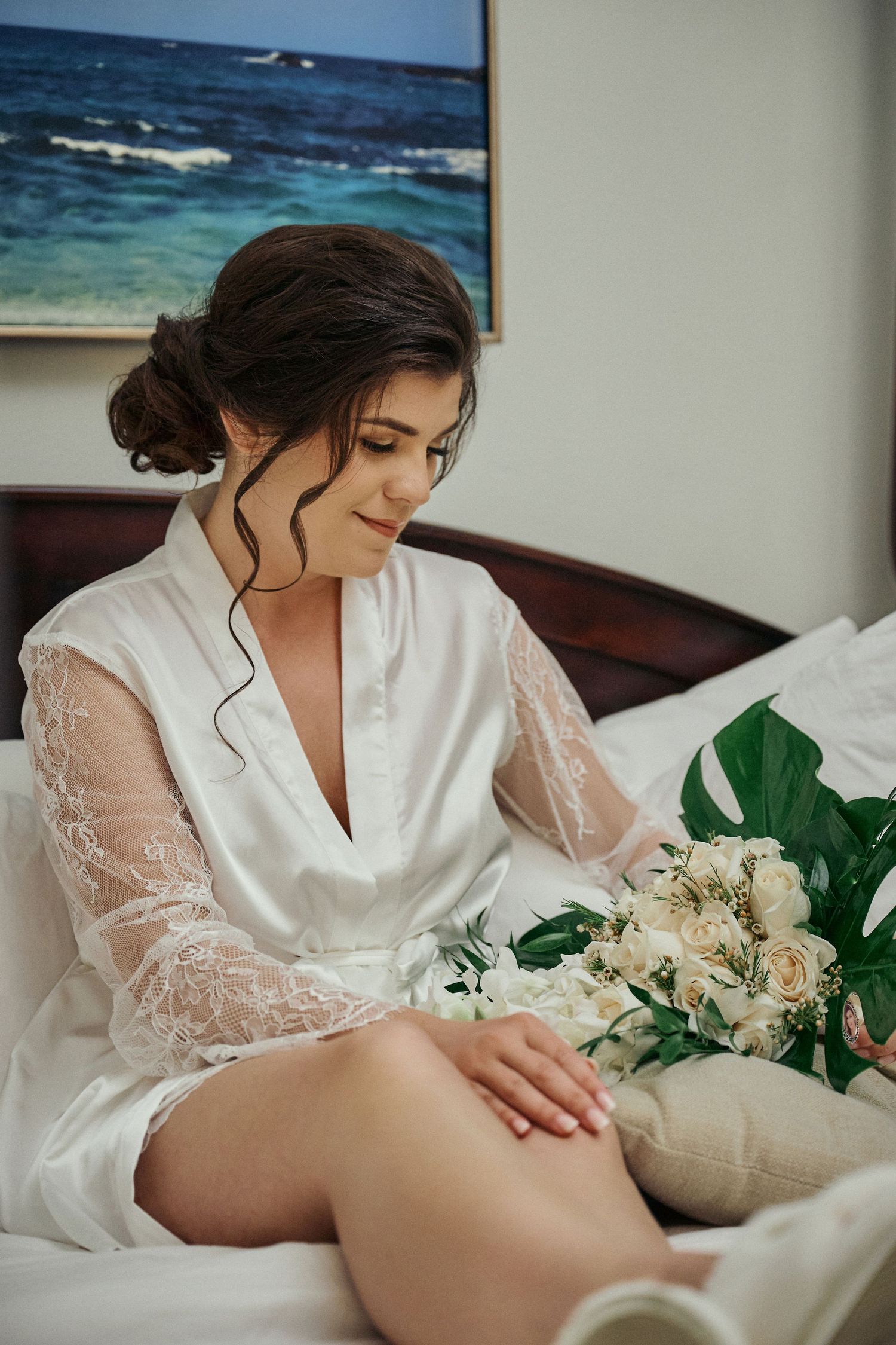 Elegant bridal boudoir scene with white lace robe and cream roses against ocean painting backdrop. Jamaican Photographer
