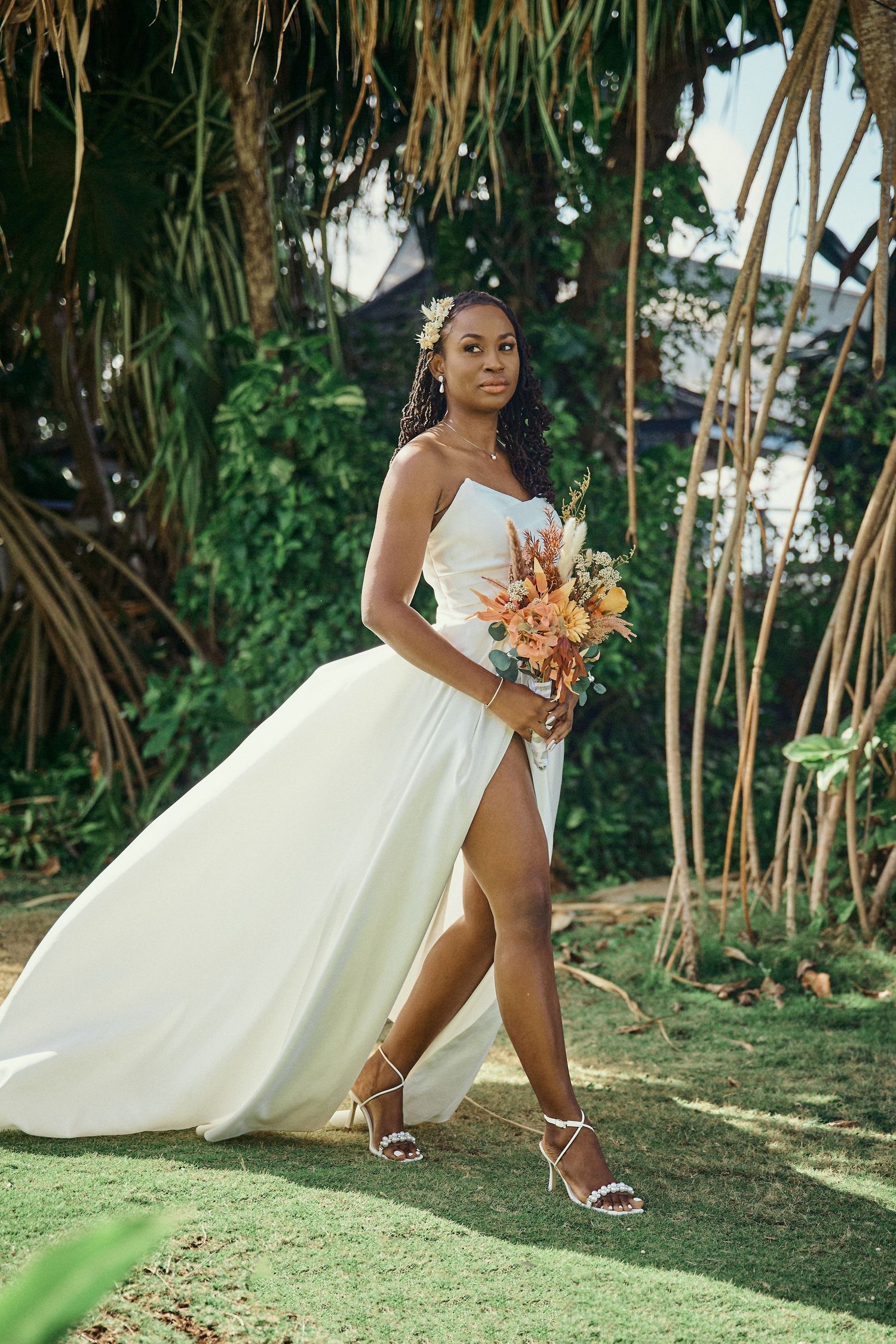 A bride in a flowing white wedding gown with a side slit holds a peach bouquet while posing in a Jamaican Photographer
