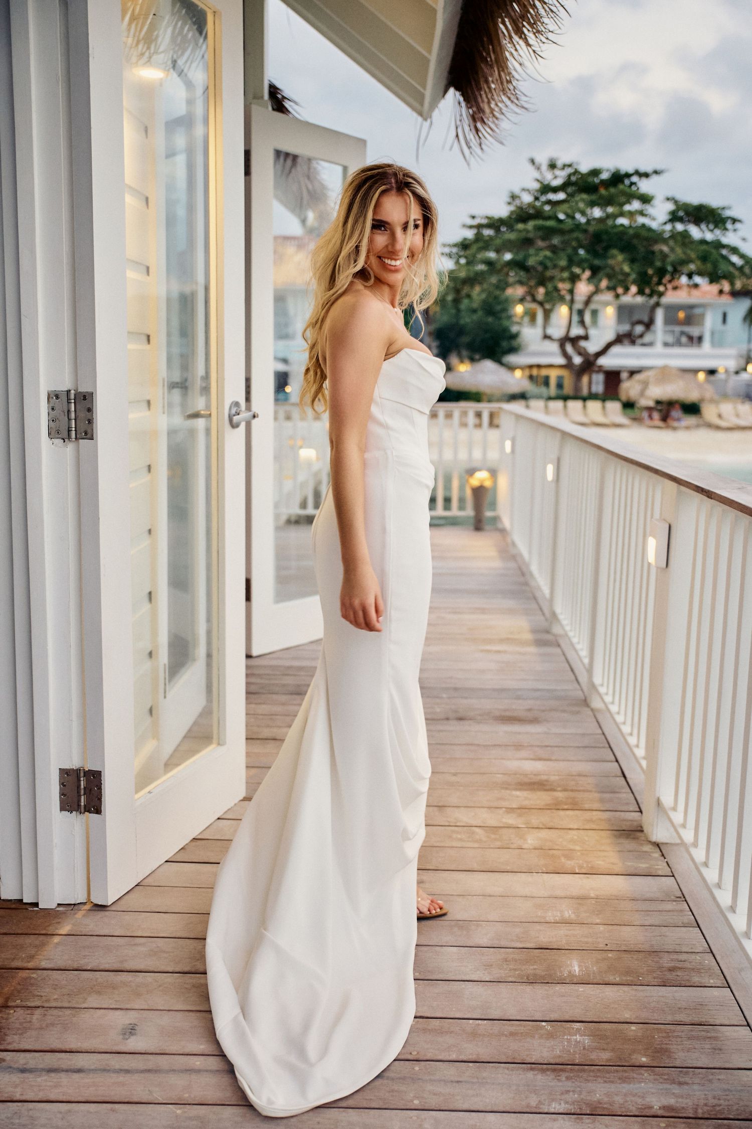 A white strapless wedding dress is showcased on a wooden deck balcony with palm trees and ocean Jamaica Wedding Photographer