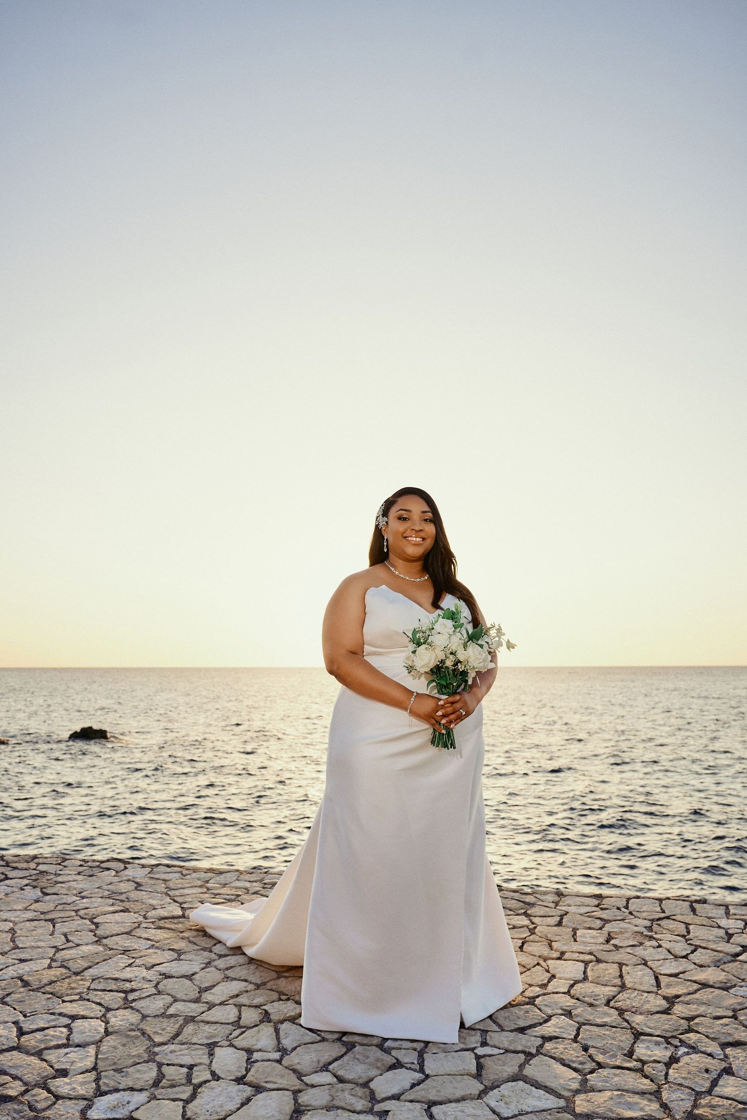 A bride in an elegant white wedding dress holds a bouquet while standing on a stone patio Jamaican Photographer