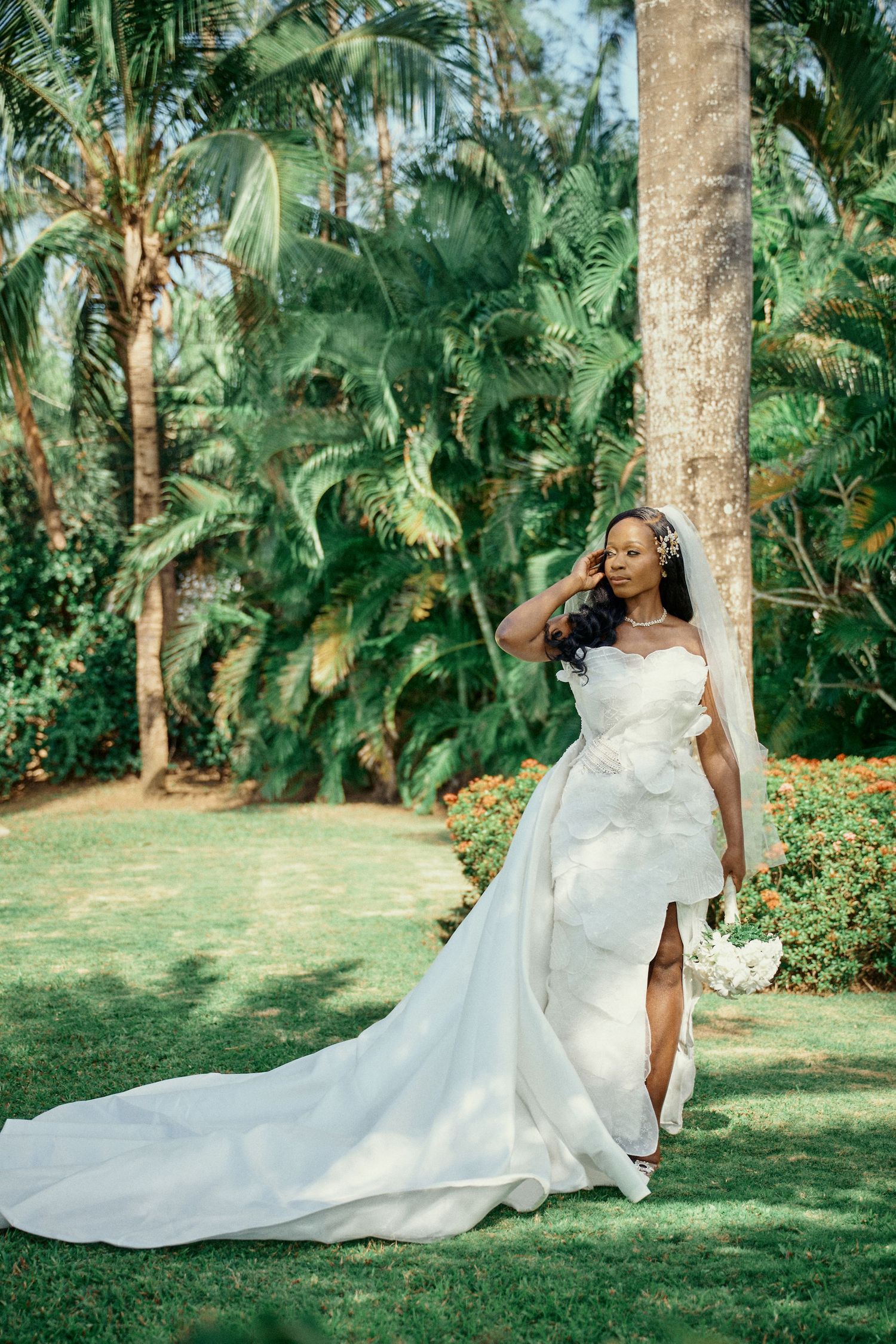Beautiful bride in flowing white wedding gown poses gracefully on lush tropical lawn surrounded Jamaica Wedding Photographer