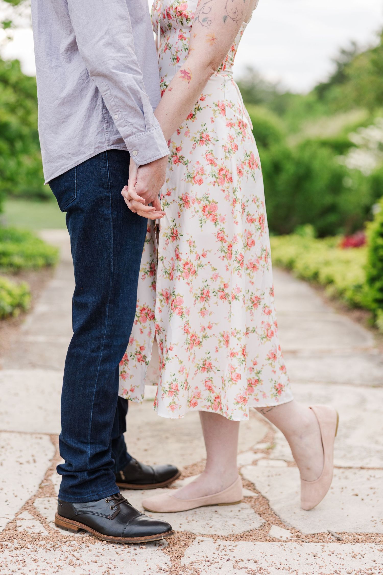 Couple holding hands romantically on garden path with person wearing floral dress and flats and other in jeans and boots at Cantigny Park