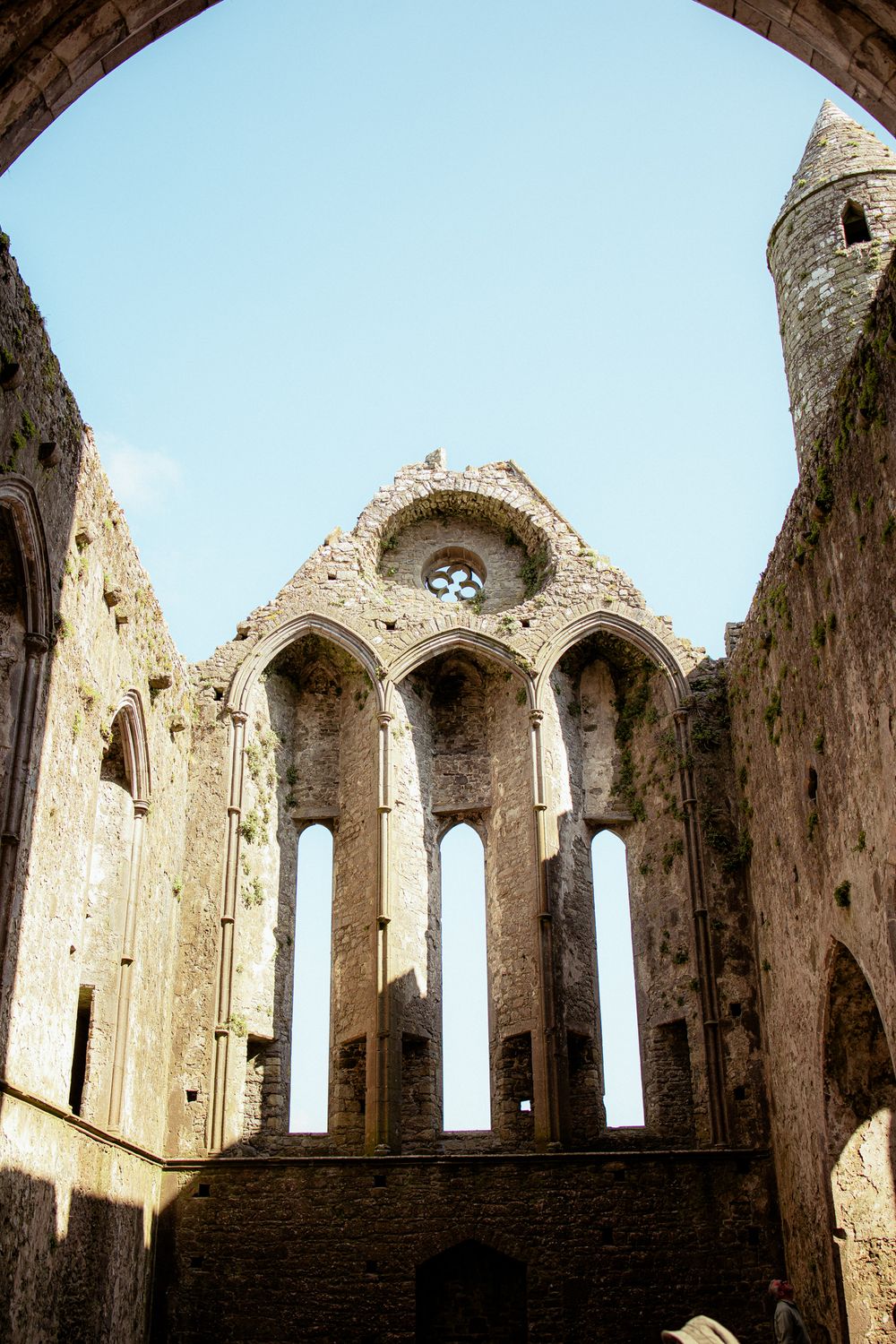 Ancient stone church ruins with gothic arches and windows against blue sky viewed through architectural framing.