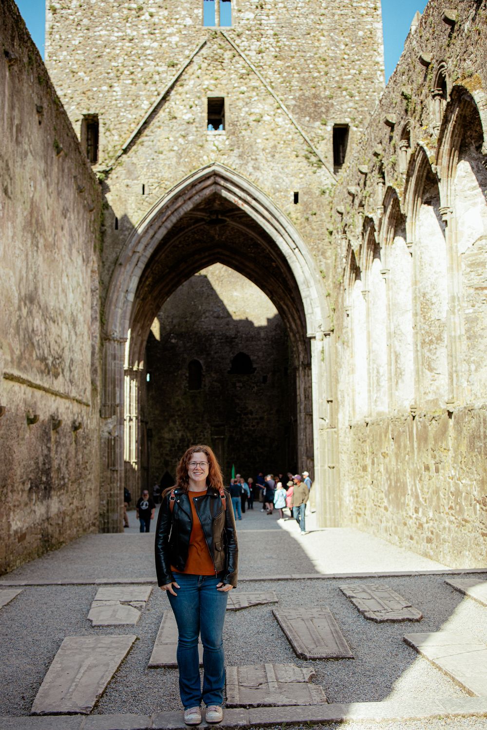Tourist stands in stone archway corridor of ancient historic ruins with gothic architecture and vaulted ceilings.