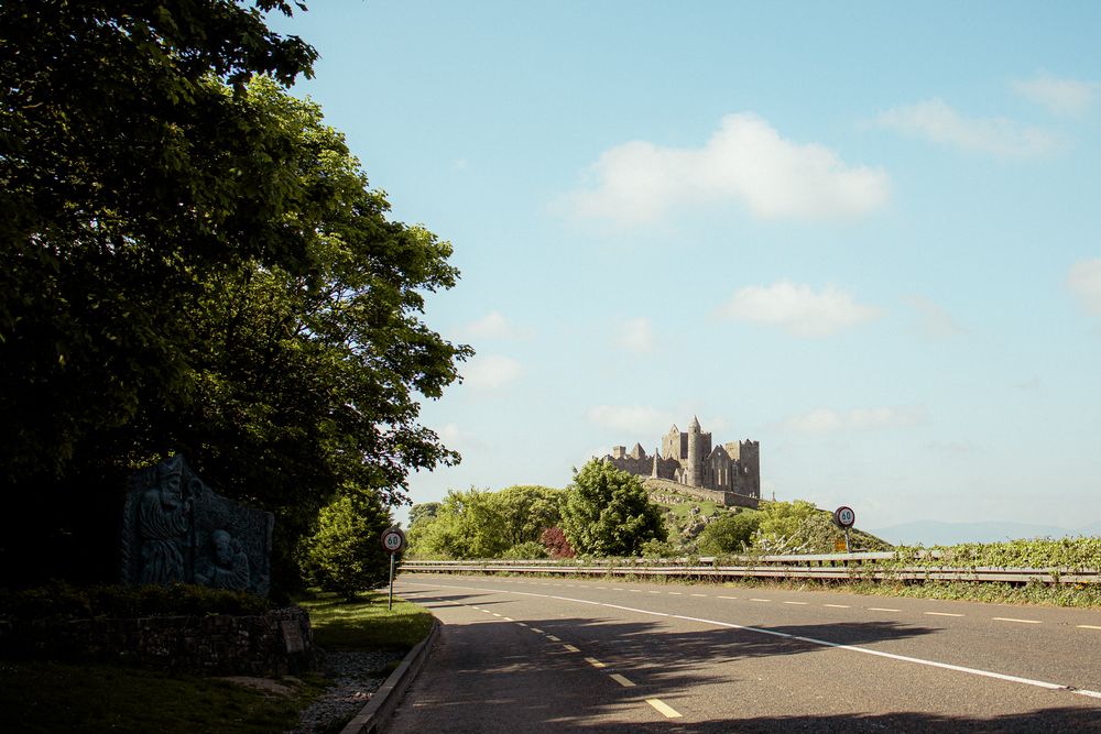 A winding road leads to Bamburgh Castle perched on a hilltop in Northumberland, England on a sunny summer day.