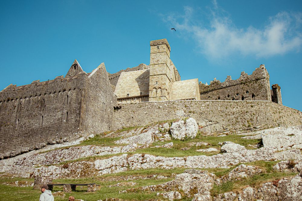 Ancient stone walls and towers of the Rock of Cashel rise against blue sky in County Tipperary, Ireland.