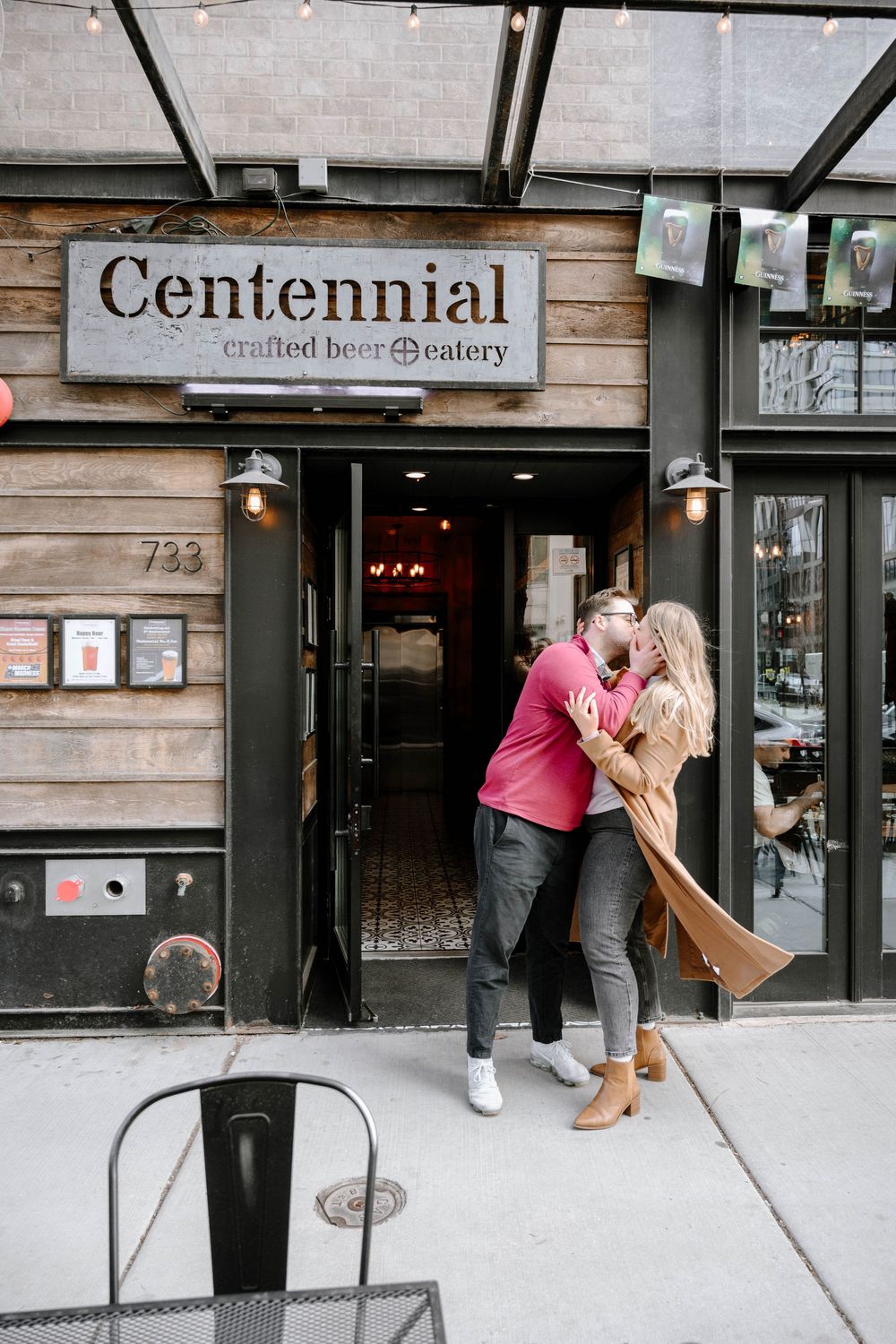 A romantic moment shared outside the entrance of Centennial craft beer eatery on a city sidewalk.