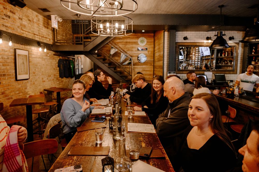 A cozy restaurant interior with exposed brick walls, wooden beams, and a group gathered around a long dining table.
