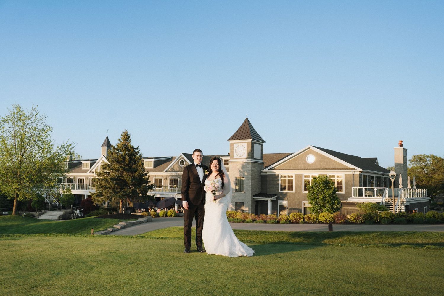 Wedding couple pose on lawn with elegant building and turret in background.