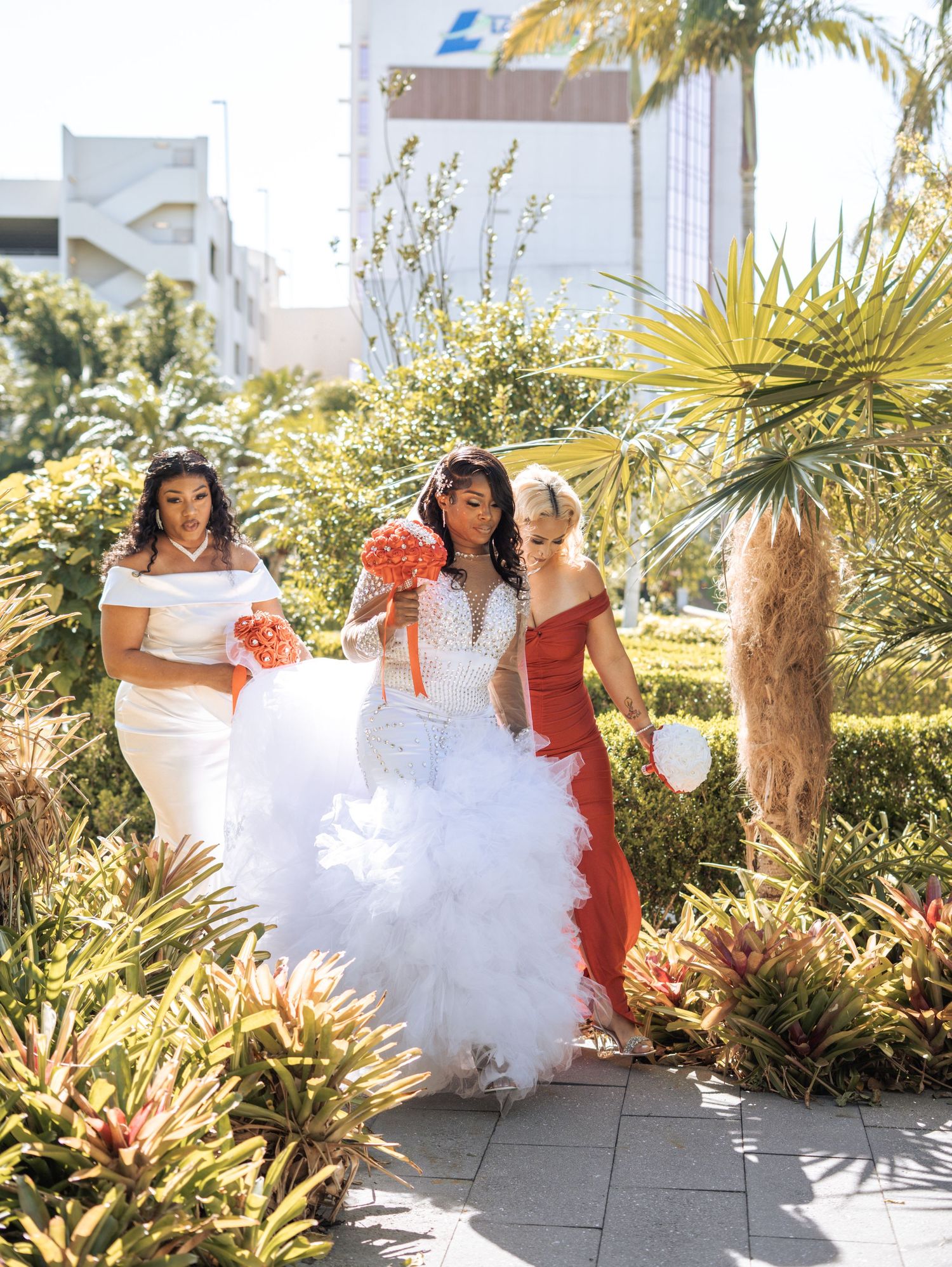 A wedding party walking through a tropical garden setting with decorative palm trees and foliage.