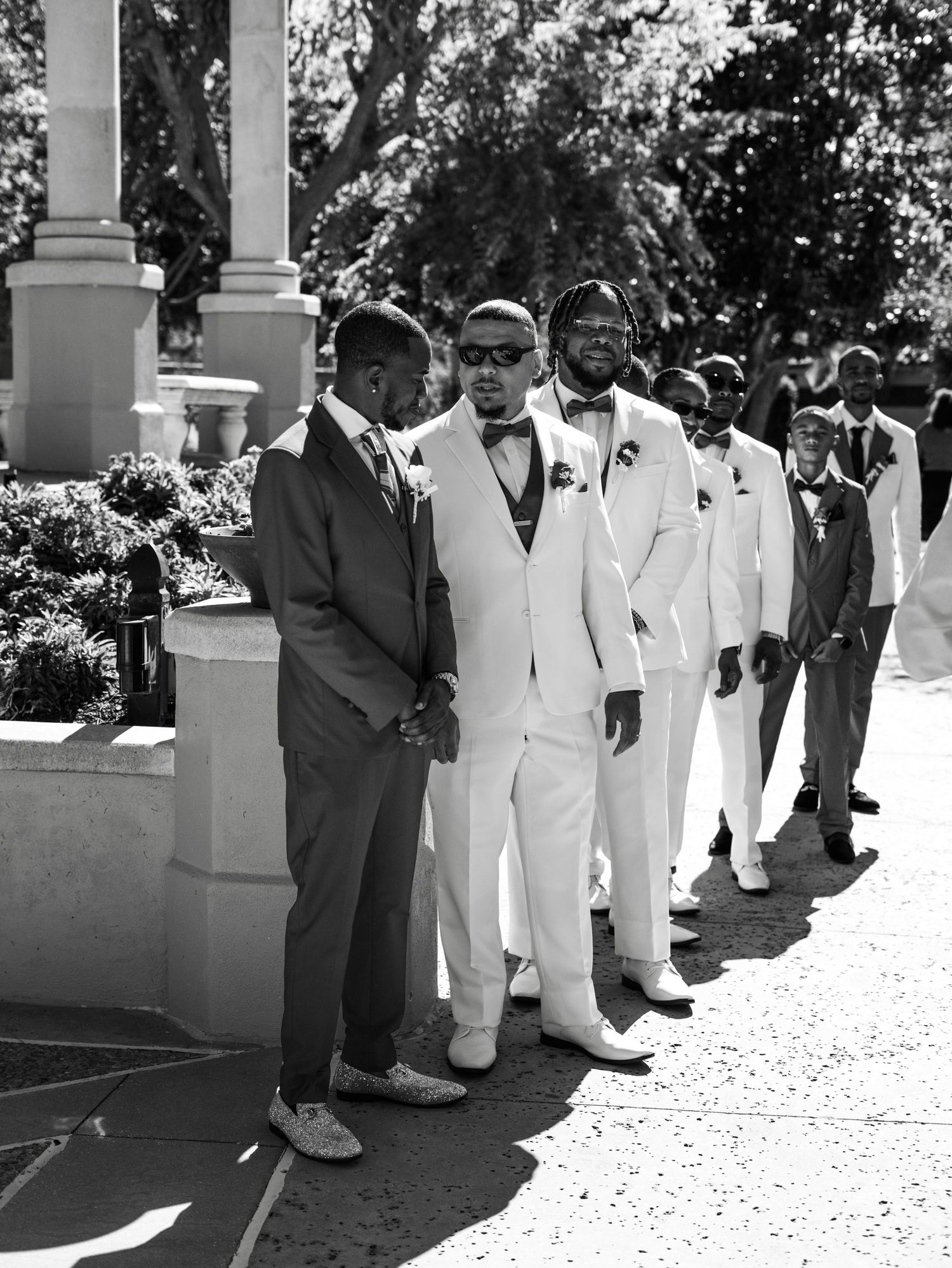 Formal wedding party groomsmen lined up in suits during outdoor ceremony.