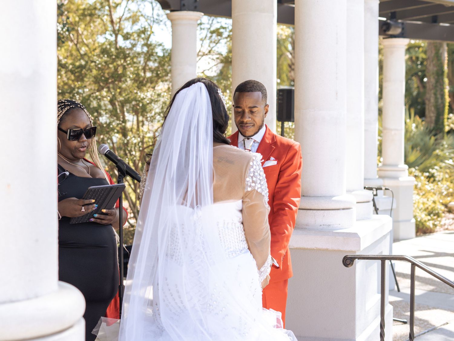 A joyful wedding ceremony takes place between two people at an elegant outdoor venue with white columns.