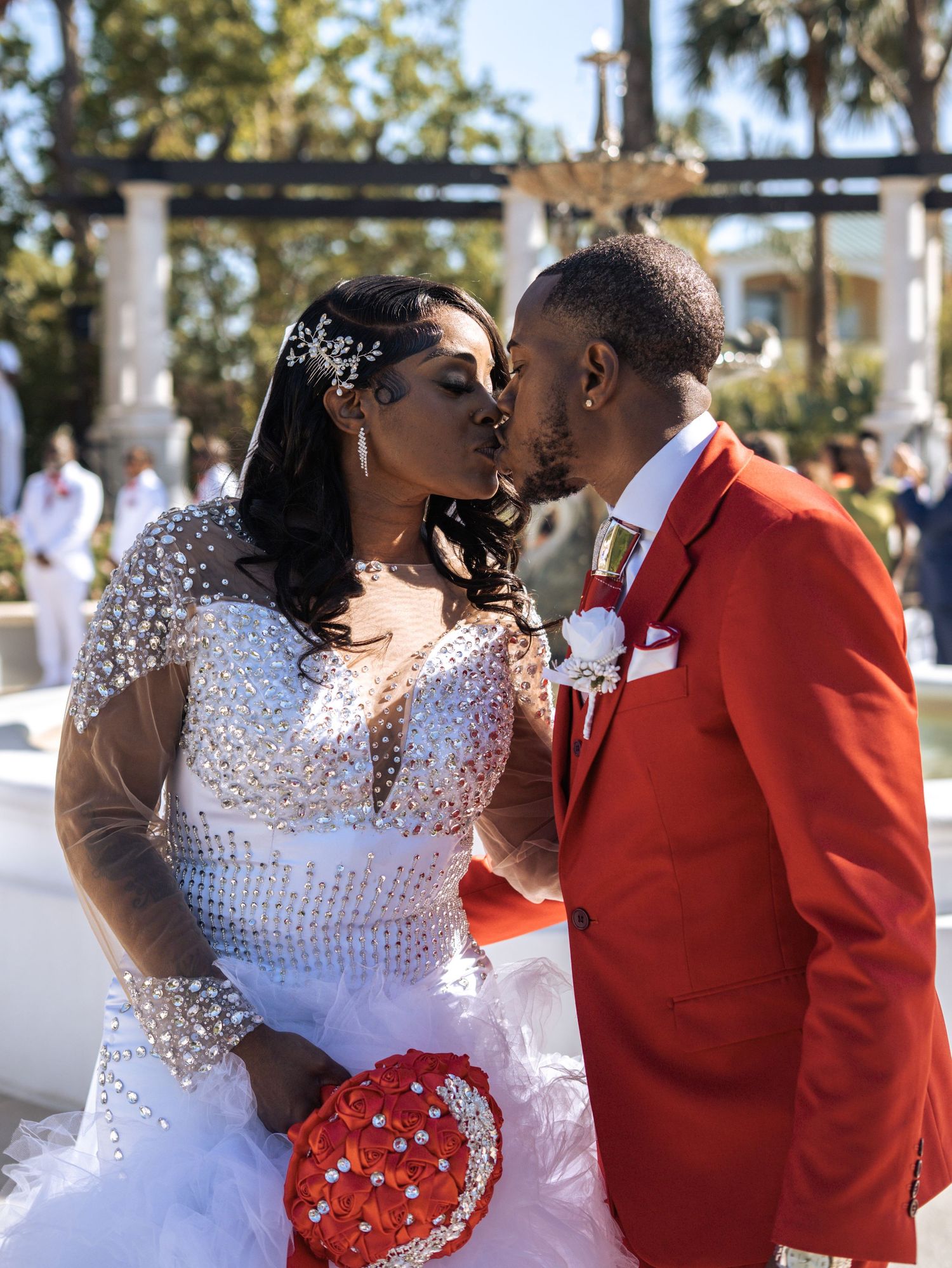 A romantic wedding moment captured in an outdoor garden setting with decorative columns.