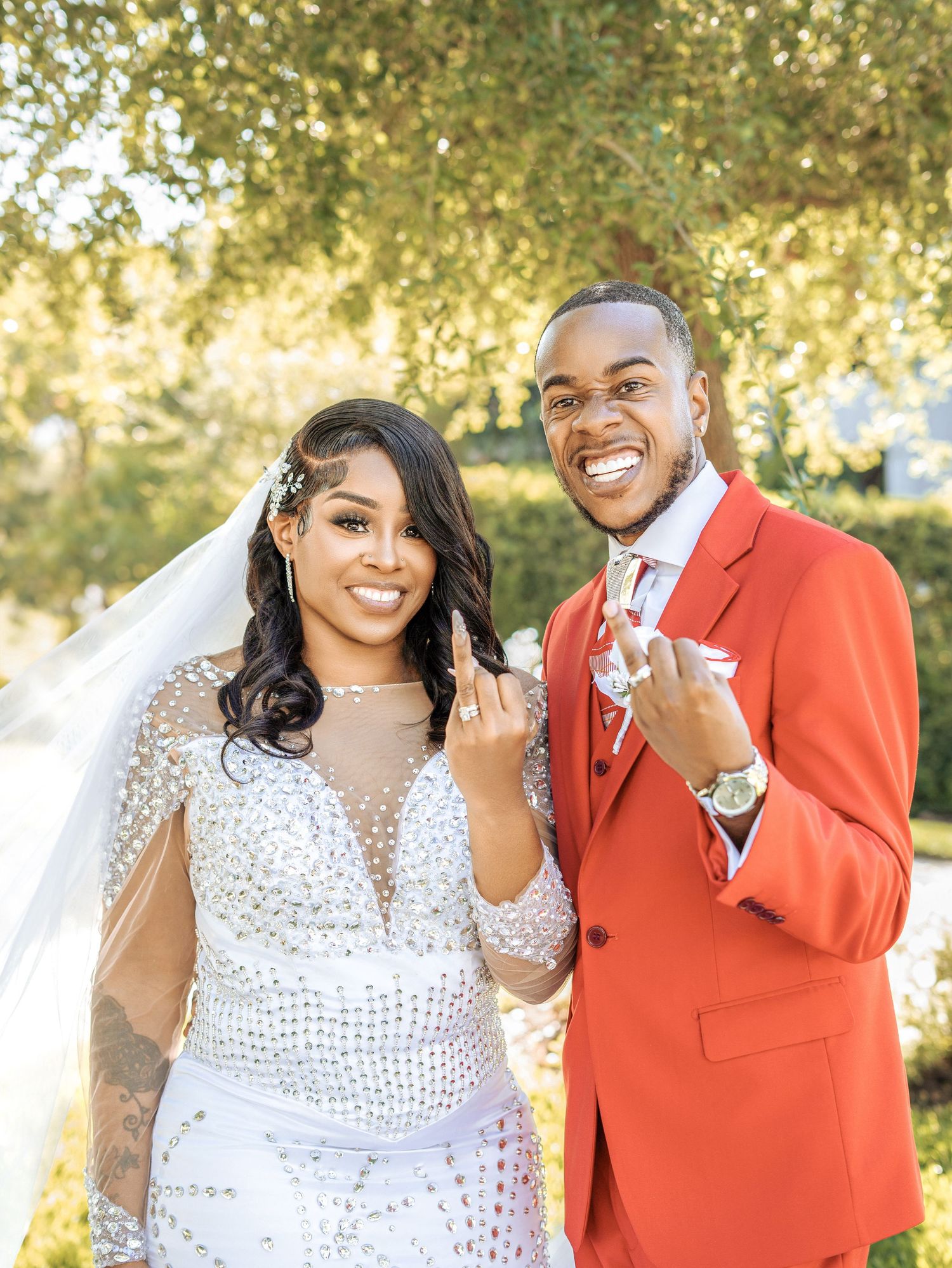A newlywed couple celebrating with their rings in an outdoor setting with glowing natural light and trees in background.