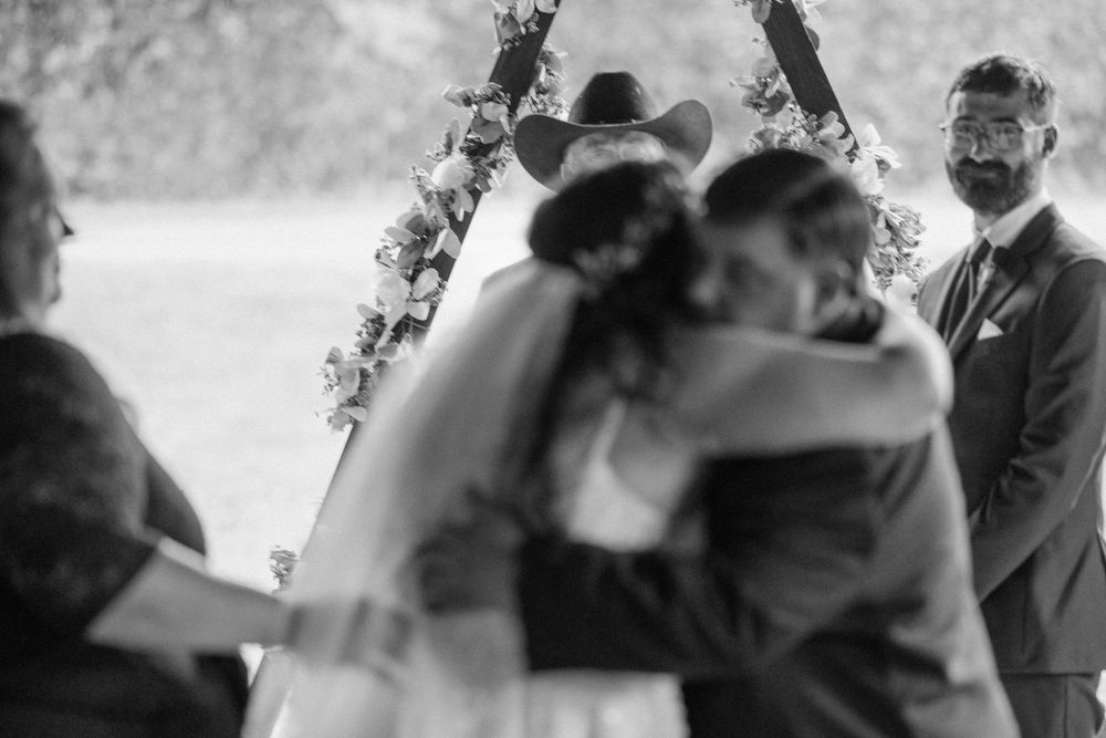 Black and white photo of a wedding ceremony moment under a floral arch.