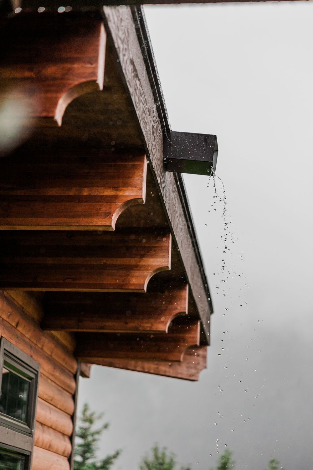 Detail shot of rustic wooden eaves and rain drops against an overcast sky.