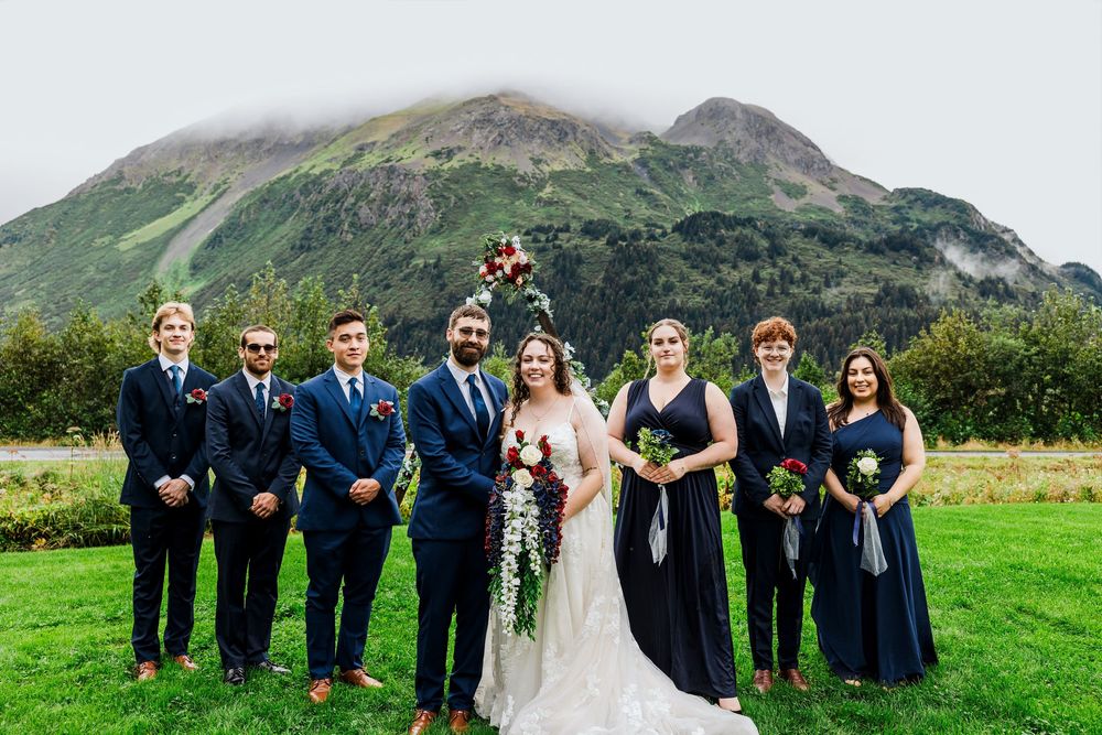 Wedding party poses in formal attire against a stunning mountain landscape backdrop.