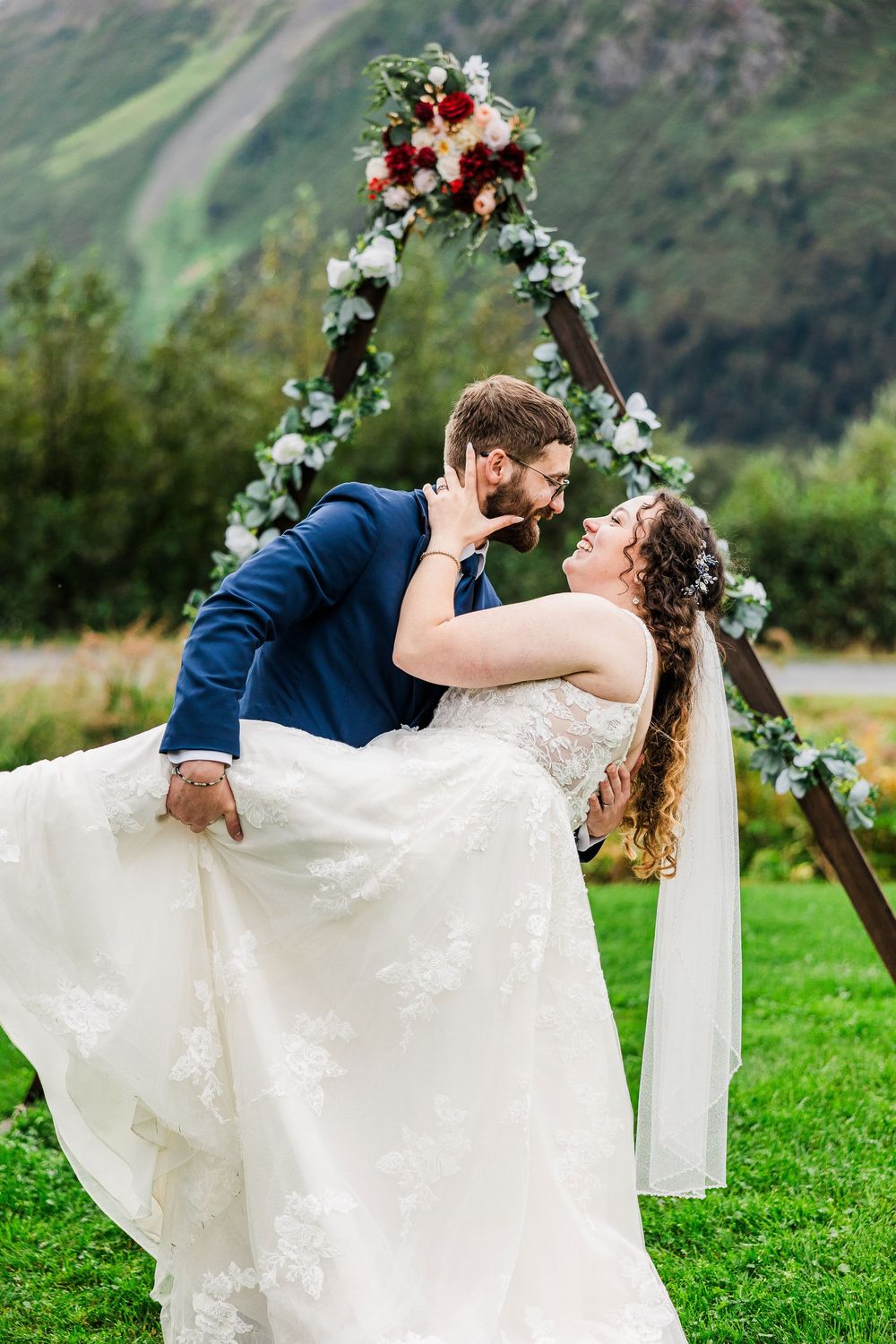 Romantic dip pose under floral arch with mountain vista in background.