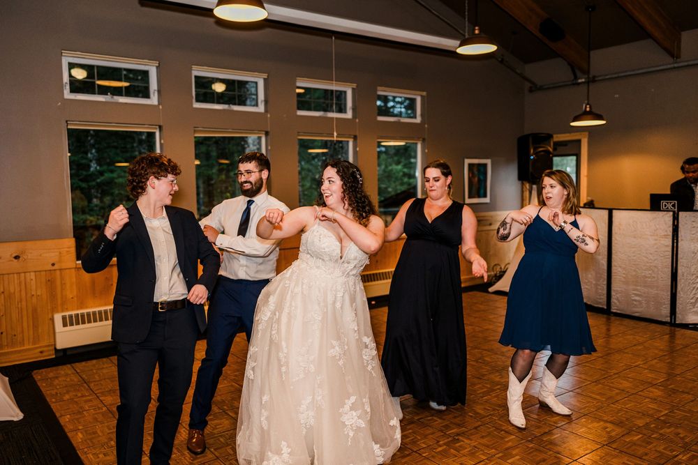 Wedding party dancing together on a wooden dance floor during reception celebrations.